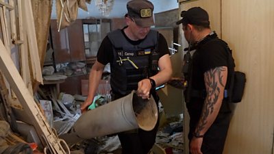 A bomb disposal expert removes part of a bomb that had landed in a living-room