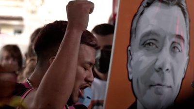 A protester with his fist in the air, next to a placard with a picture of Dom Phillips.