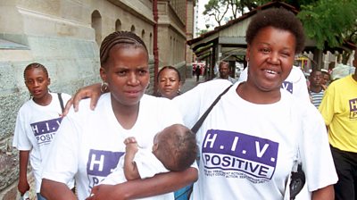 Two women wearing HIV Positive t-shirts smile at the camera