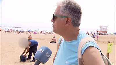 A man talking to TV crew while a man steal a bag on the beach