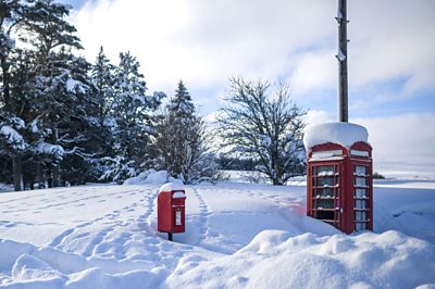A red post box and phone box poke out of very deep snow