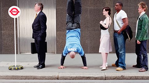 Man doing a handstand in a queue at a temporary bus stop.