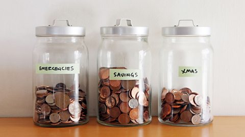 Glass jars filled with coins and labels for emergencies, savings and Christmas.
