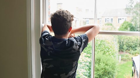 boy looking out of window into his back garden