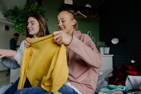 Two teenage girls swap clothes. One is holding a yellow jumper