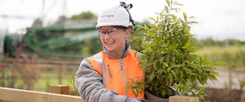 Emma at work, smiling and holding a plant.