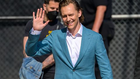 A picture of actor Tom Hiddleston waving in the street.