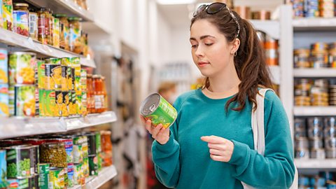 woman in a supermarket looks at a tin