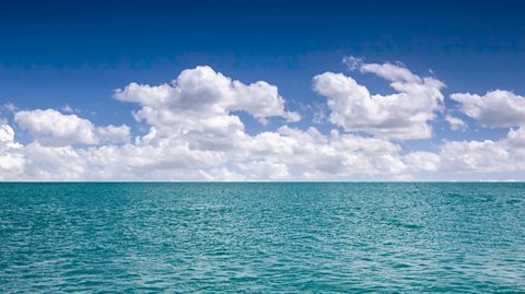 A blue ocean with clouds in a blue sky.