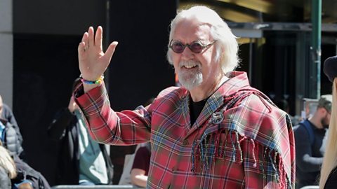 Comedian Billy Connoly waving at a tartan parade in New York City.