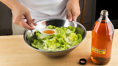 A bowl of salad with a person adding apple cider vinegar to it 