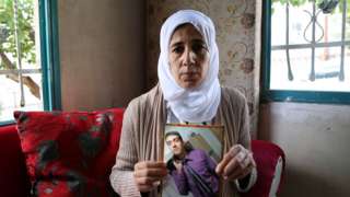 Image shows woman holding up picture of Hisham al-Sayed