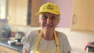 Caroline Dove in a yellow apron and hat that reads Caroline's Hot Food.
