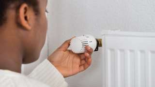 Woman adjusting temperature of radiator using thermostat
