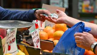 A trader gives change to a customer at a market stall in London on 12 May 2022