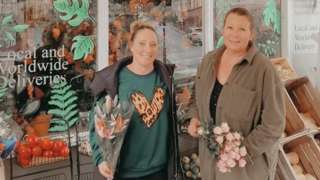 Two women standing outside a florist holding bunches of flowers