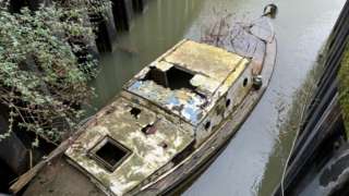 A boat slowly sinking with a broken roof and weeds growing from it
