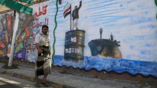 A Yemeni man walks past a mural showing a Houthi fighter stopping an Israeli ship in the Red Sea, in Sanaa, Yemen (19 February 2024)