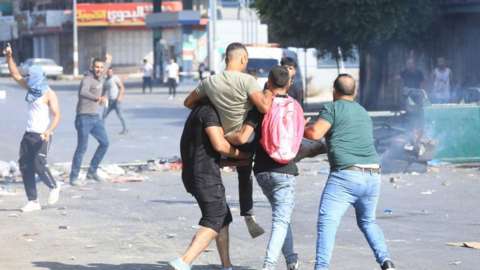 Palestinians carry a wounded man during clashes with Israeli troops during a raid in the West Bank city of Nablus, 09 August 2022.