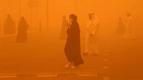 Pedestrians cross a road amid a severe dust storm in Kuwait City, as the increasingly frequent weather phenomenon enveloped parts of the Middle East