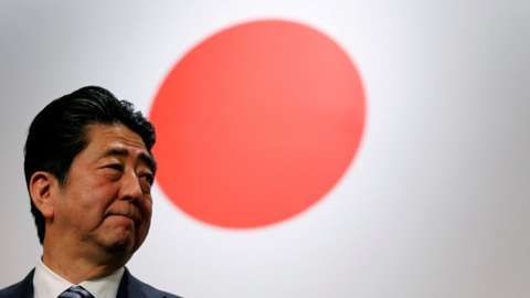 Japan's Prime Minister Shinzo Abe stands in front of Japan's national flag