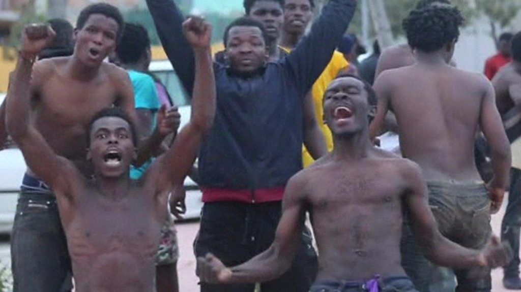Men in Ceuta without shirts kneel on the ground and throw hands in the air in celebration