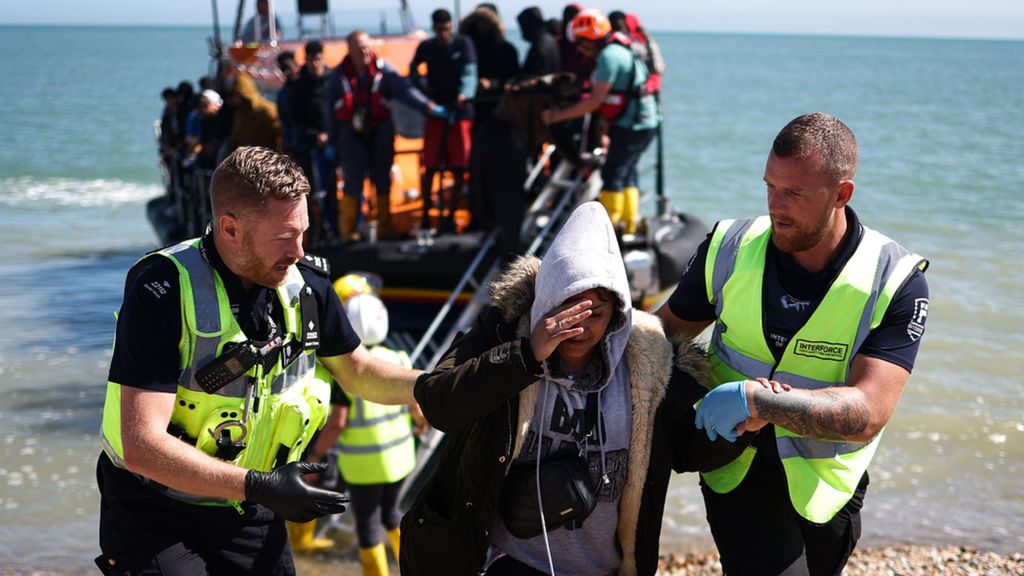 An interforce officer and a border force officer help a woman on the beach at Dungeness on the southeast coast of England, on 16 August 2023