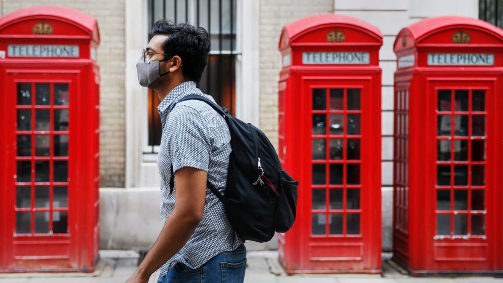 Man wearing a mask walks past phone boxes