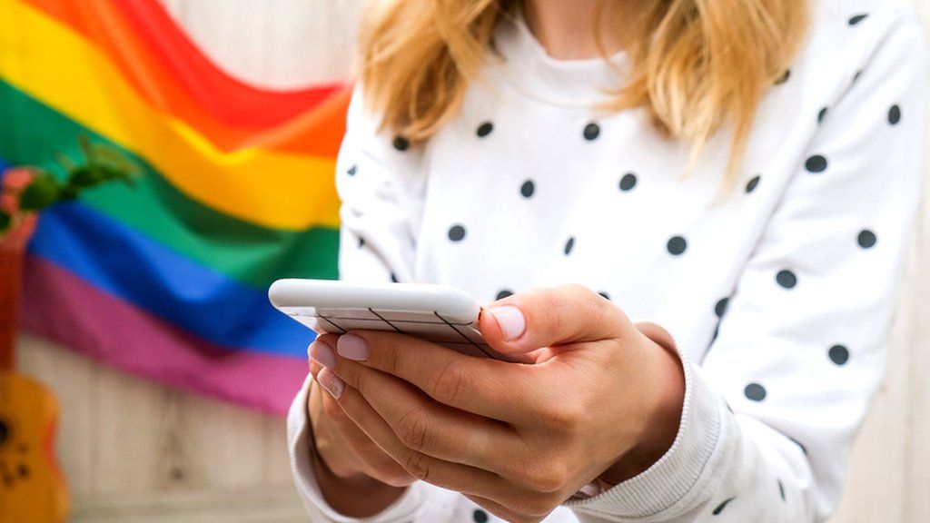 Anonymous person holding phone with pride flag in background