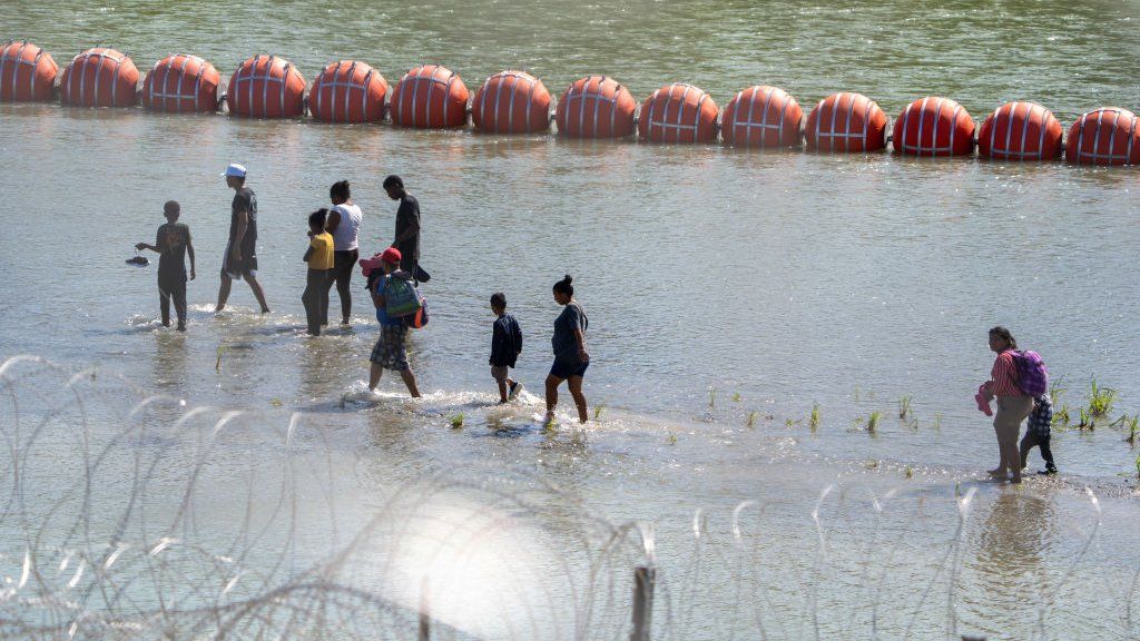 Migrants walk by a string of buoys placed on the water along the Rio Grande border with Mexico in Eagle Pass, Texas, on July 15, 2023, to prevent illegal immigration entry to the US.