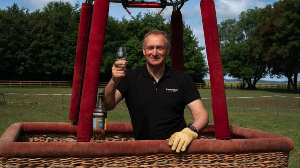 Sir David Hempleman-Adams standing in the basket of a hot air balloon holding a glass