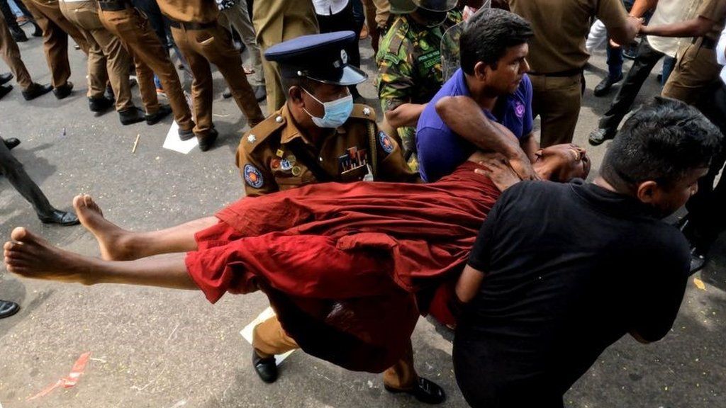 A Sri Lankan monk is carried out by police officers after being attacked by government supporters