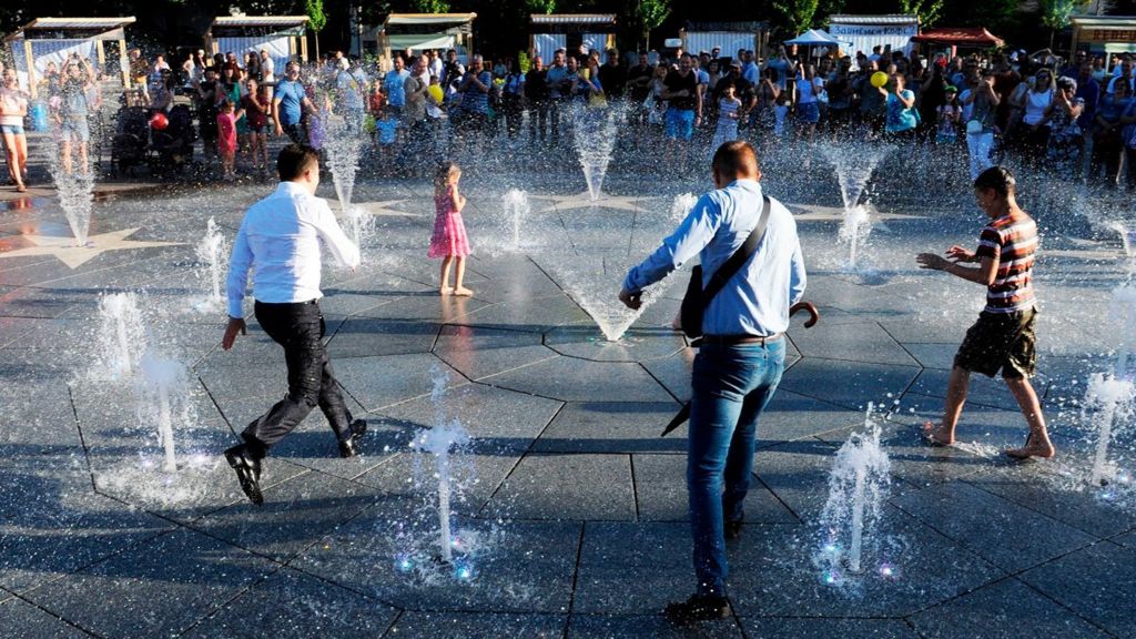 President Volodymyr Zelensky (L) and children refresh themselves in a fountain during his first official visit to Mariupol on 15 June 2019