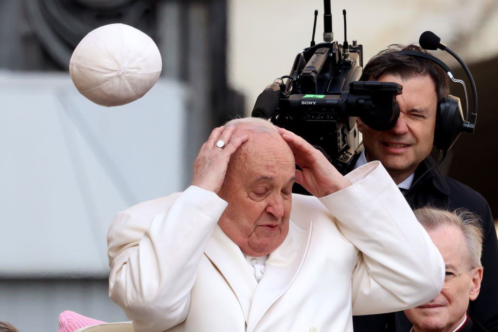 The cap of Pope Francis is blown off his head