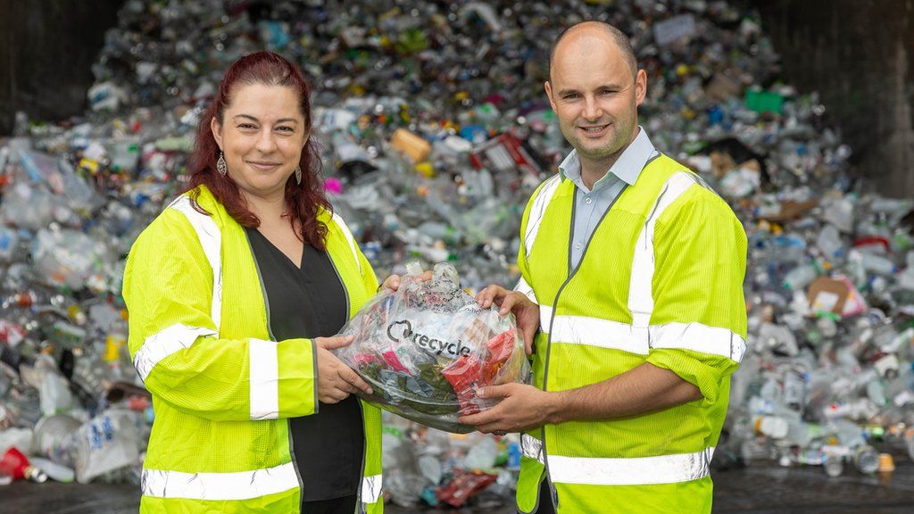 A man and woman wearing high visibility jackets holding plastic waste