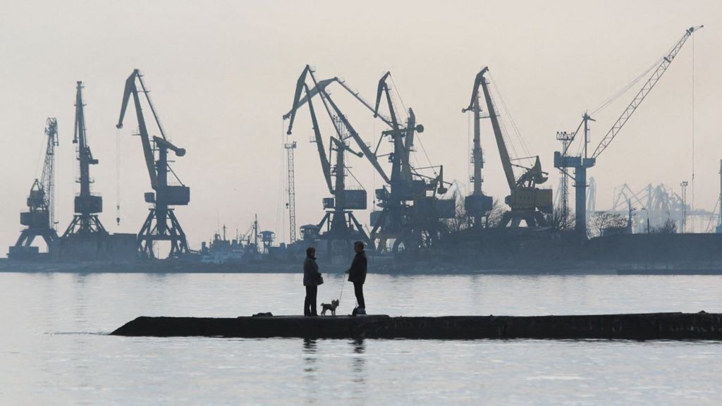 A couple walks a dog on a pier at a coast of the Sea of Azov in Ukraine's industrial port city of Mariupol on February 23, 2022