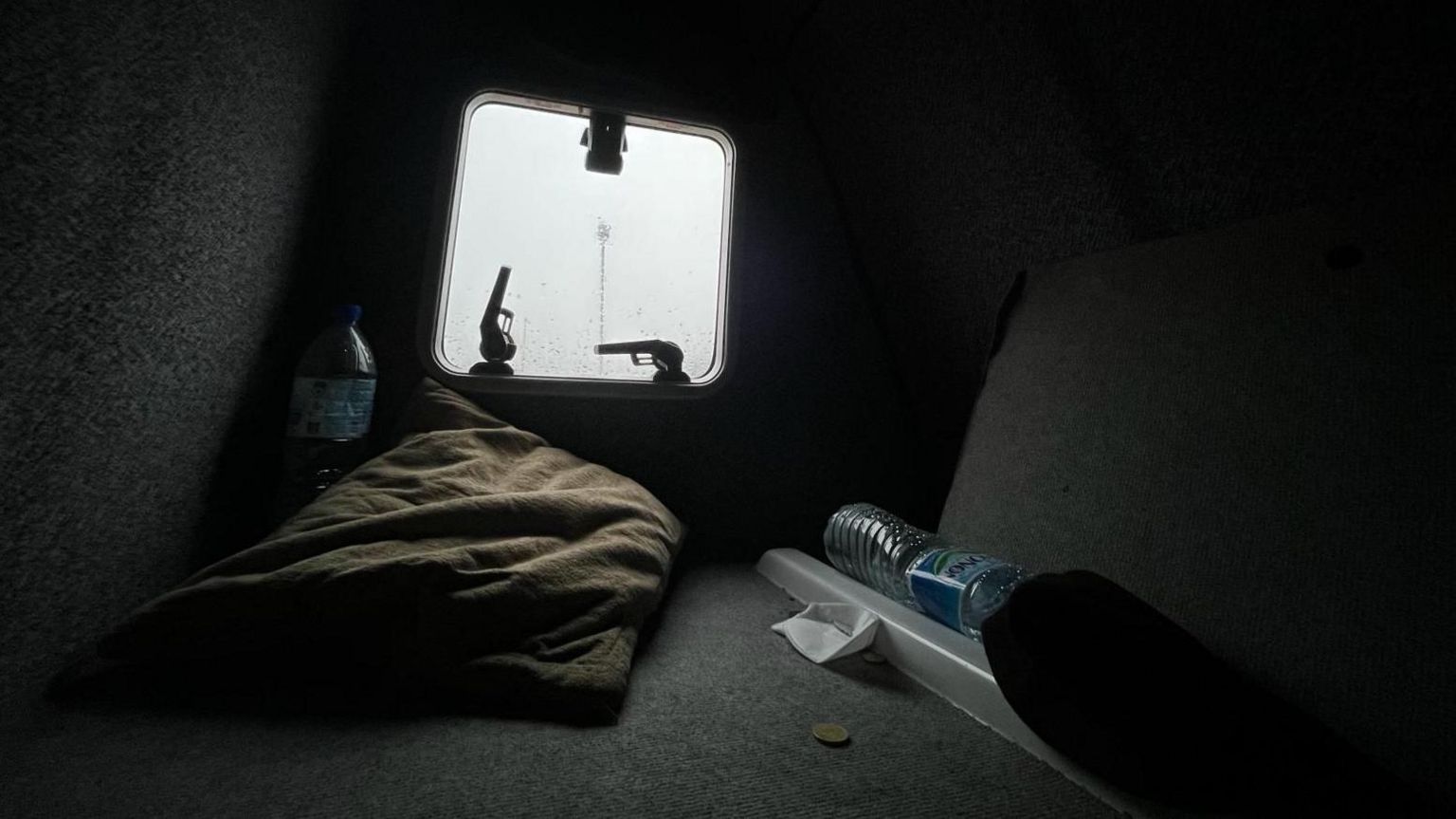 The back of a van with a window, a pillow, water bottle and two guns 