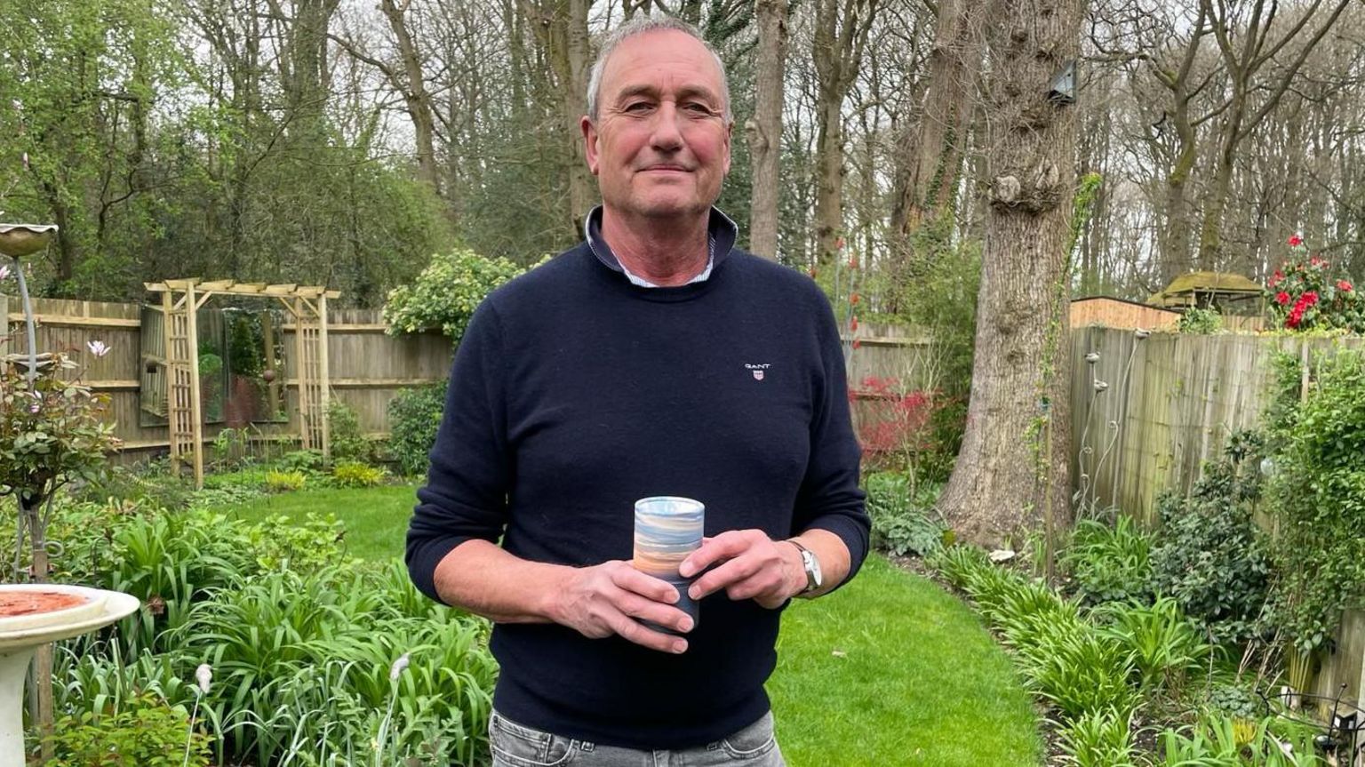 Keith Rudd holding the ashes in a garden