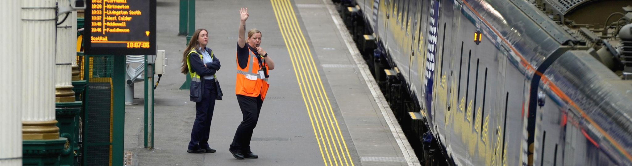 Train staff wave off a train on an empty platform at Waverley Station in Edinburgh