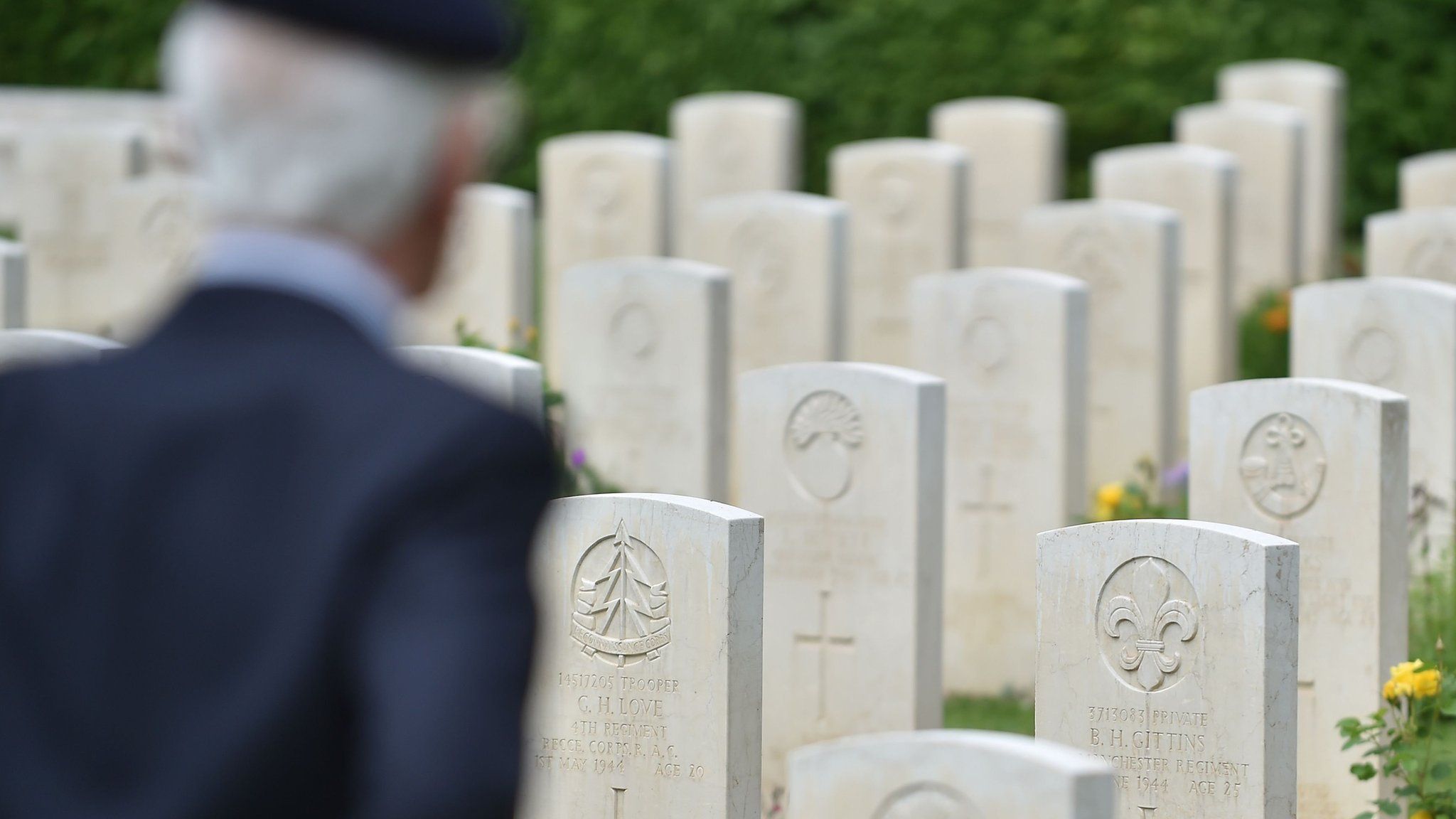 A veteran in uniform stands before war graves