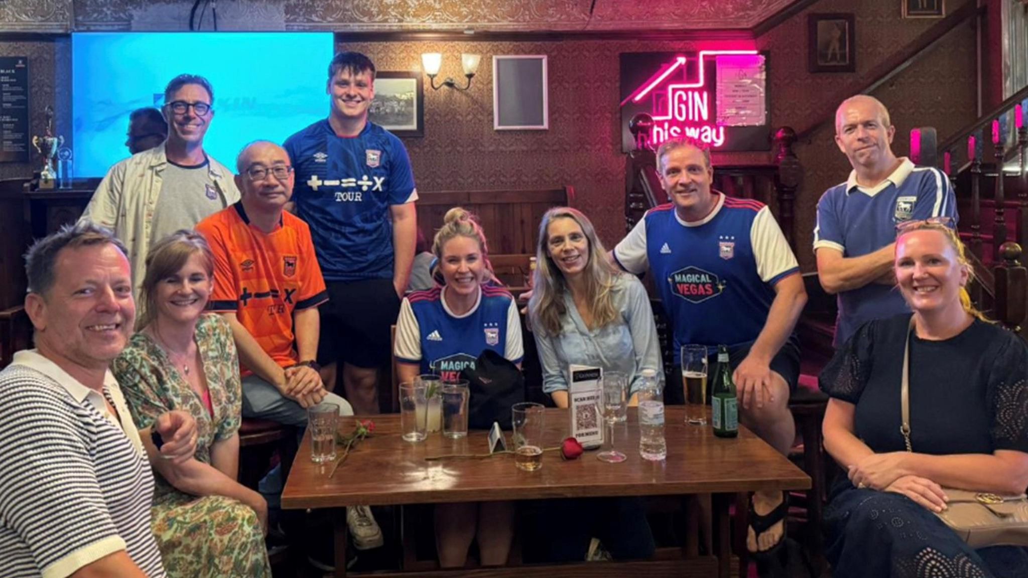 Ten football fans - several wearing Ipswich Town replica shirts - crowded around a table in a bar