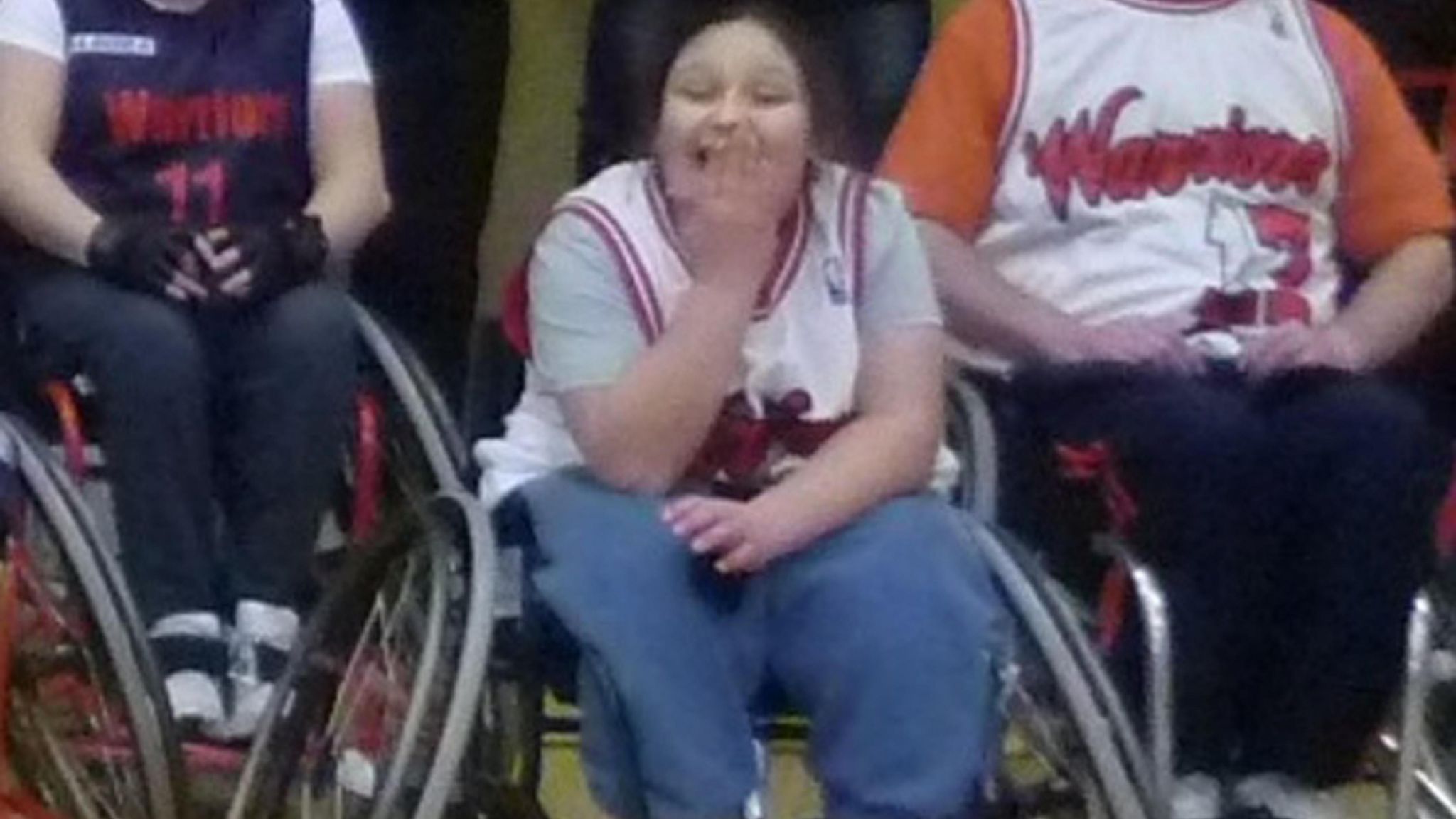 Kaylea in a wheelchair with a big smile and a hand over her mouth.