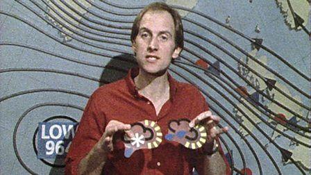 Blue Peter presenter Simon Groom, standing in front of an old-fashioned weather chart, holding some magnetic weather symbols.