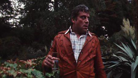 oliver reed wanders through his overgrown garden, holding a glass of liquid