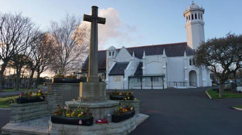 A cross memorial outside a white church