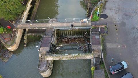 Aerial view of river gate and weir with lots of debris caught in gate