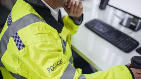 A stock image of a police officer sat at a desk