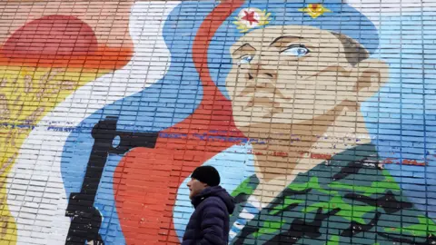 A man walks in front of a patriotic mural with a Russian soldier in Moscow