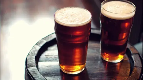 Two pints of beer bitter on wooden barrel in London pub.