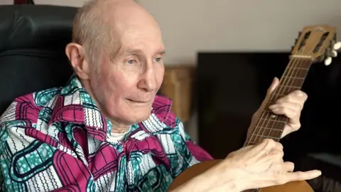 Care home resident John playing a guitar